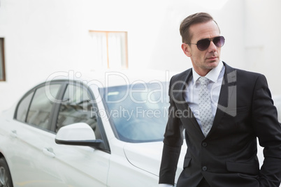 Serious businessman leaning against his car