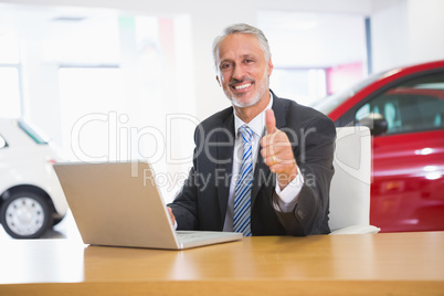 Smiling businessman giving thumbs up using his laptop