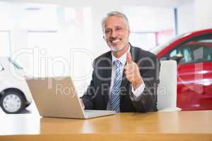 Smiling businessman giving thumbs up using his laptop