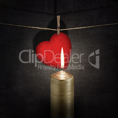 burning candle and red paper heart on a rope