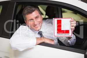 Man holding a learner driver sign sitting behind the wheel