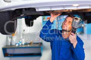 Mechanic examining under the car with torch