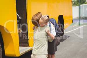 Mother hugging her daughter by school bus