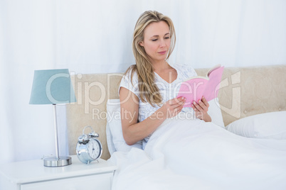 Concentrated blonde reading a book in bed