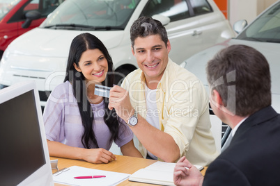 Smiling couple holding credit card to buy a car