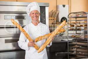 Smiling baker holding three baguettes