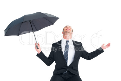 Businessman sheltering under black umbrella testing