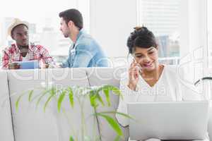 Businesswoman phoning and using laptop on couch