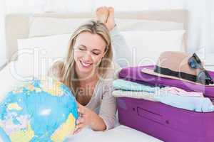 Smiling blonde lying on bed looking her globe