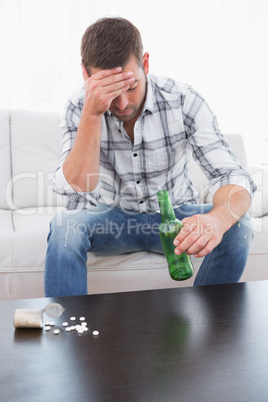 Hungover man with a beer and his medicine laid out on coffee tab