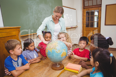 Cute pupils and teacher in classroom with globe