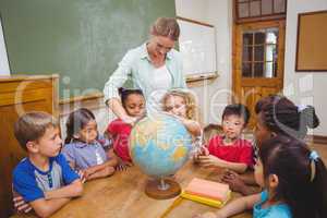 Cute pupils and teacher in classroom with globe