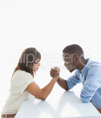 Irritated business couple arm wrestling at desk
