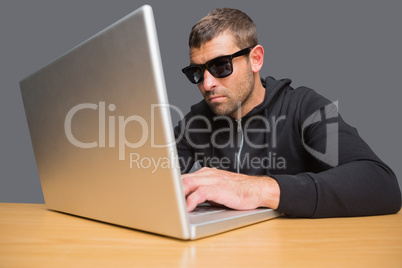 Man wearing sunglasses hacking into laptop