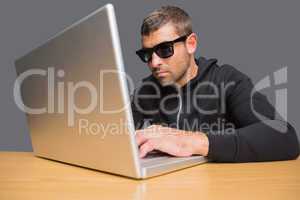 Man wearing sunglasses hacking into laptop