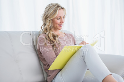 Smiling blonde on couch taking notes on notebook