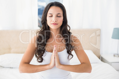 Calm brunette doing yoga on bed