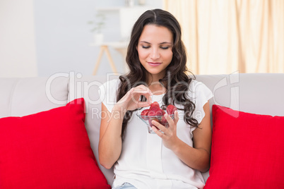 Pretty brunette eating strawberries on couch