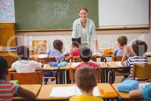 Pretty teacher talking to the young pupils in classroom