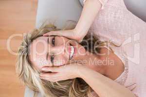 Happy blonde lying on couch with hand on head