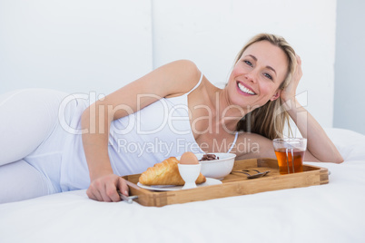 Happy blonde lying and having breakfast in bed