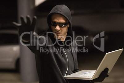 Hacker in balaclava gesturing and using laptop