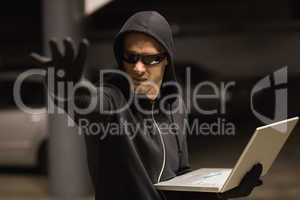 Hacker in balaclava gesturing and using laptop