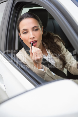 Pretty businesswoman using wing mirror to put on lipstick