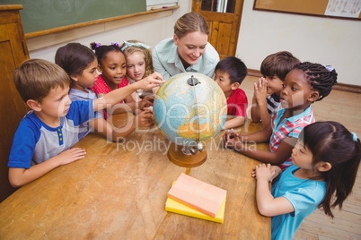 Cute pupils and teacher in classroom with globe