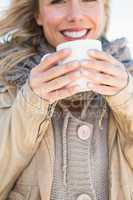 Happy blonde in warm clothes holding hot beverage