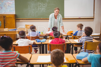 Pretty teacher talking to the young pupils in classroom