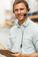 Warehouse manager wearing headset writing on clipboard