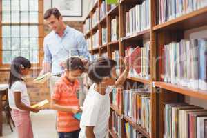 Cute pupils and teacher looking for books in library