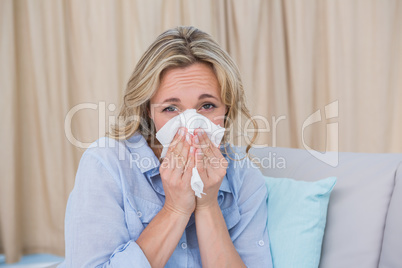 Sick blonde on couch sneezing on tissue