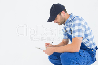 Handyman crouching while writing on clipboard