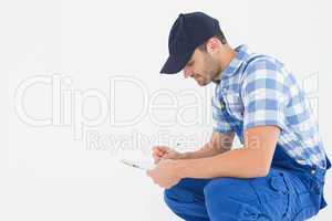 Handyman crouching while writing on clipboard