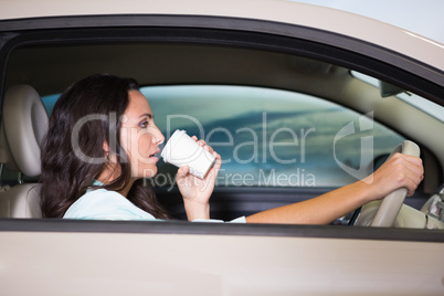 Smiling woman driving car while drinking coffee