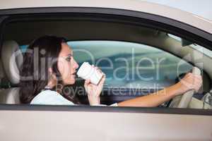 Smiling woman driving car while drinking coffee