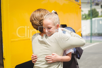 Mother hugging her daughter by school bus