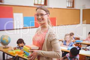 Teacher smiling at camera while holding stack of notebooks