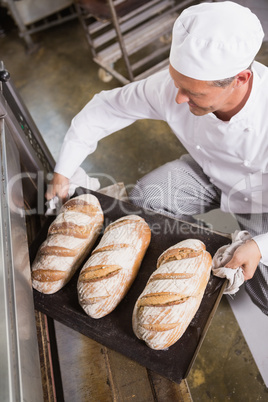 Baker taking tray of fresh bread out of oven