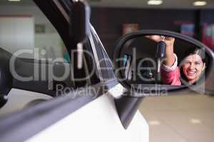 Woman showing car key in rear view mirror