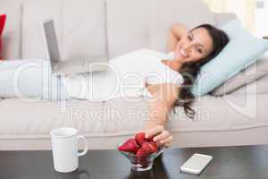 Pretty brunette lying on couch using laptop