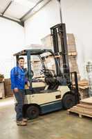 Smiling warehouse worker leaning against forklift