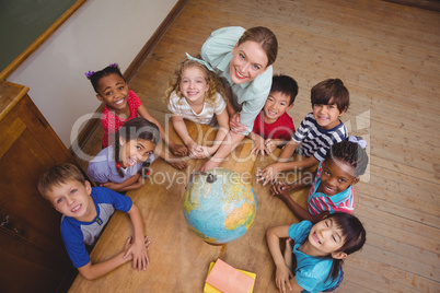 Cute pupils smiling around a globe in classroom with teacher