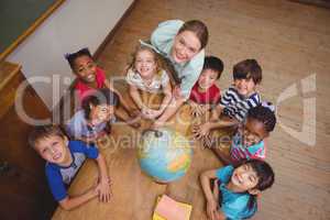Cute pupils smiling around a globe in classroom with teacher