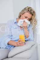 Blonde sneezing on tissue and holding glass of orange juice