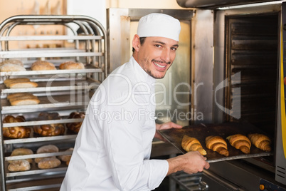 Happy baker taking out fresh croissants