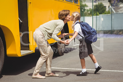 Mother kissing her daughter by school bus