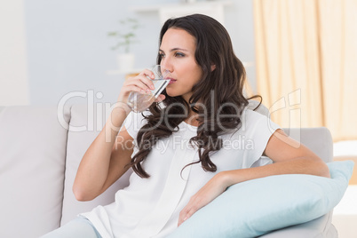Pretty brunette drinking water on couch